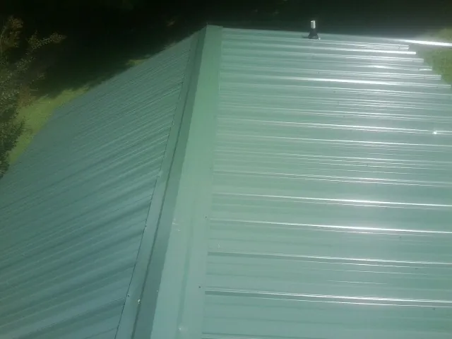 New green metal panels meeting at the ridge of a roof — Flat Roof Repair work by our crew in Hendersonville
